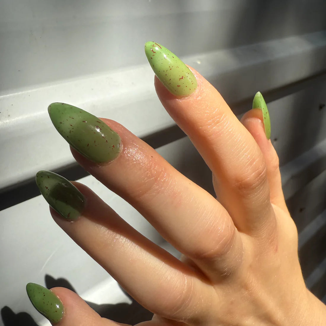 Hand with green nail polish on a reflective surface