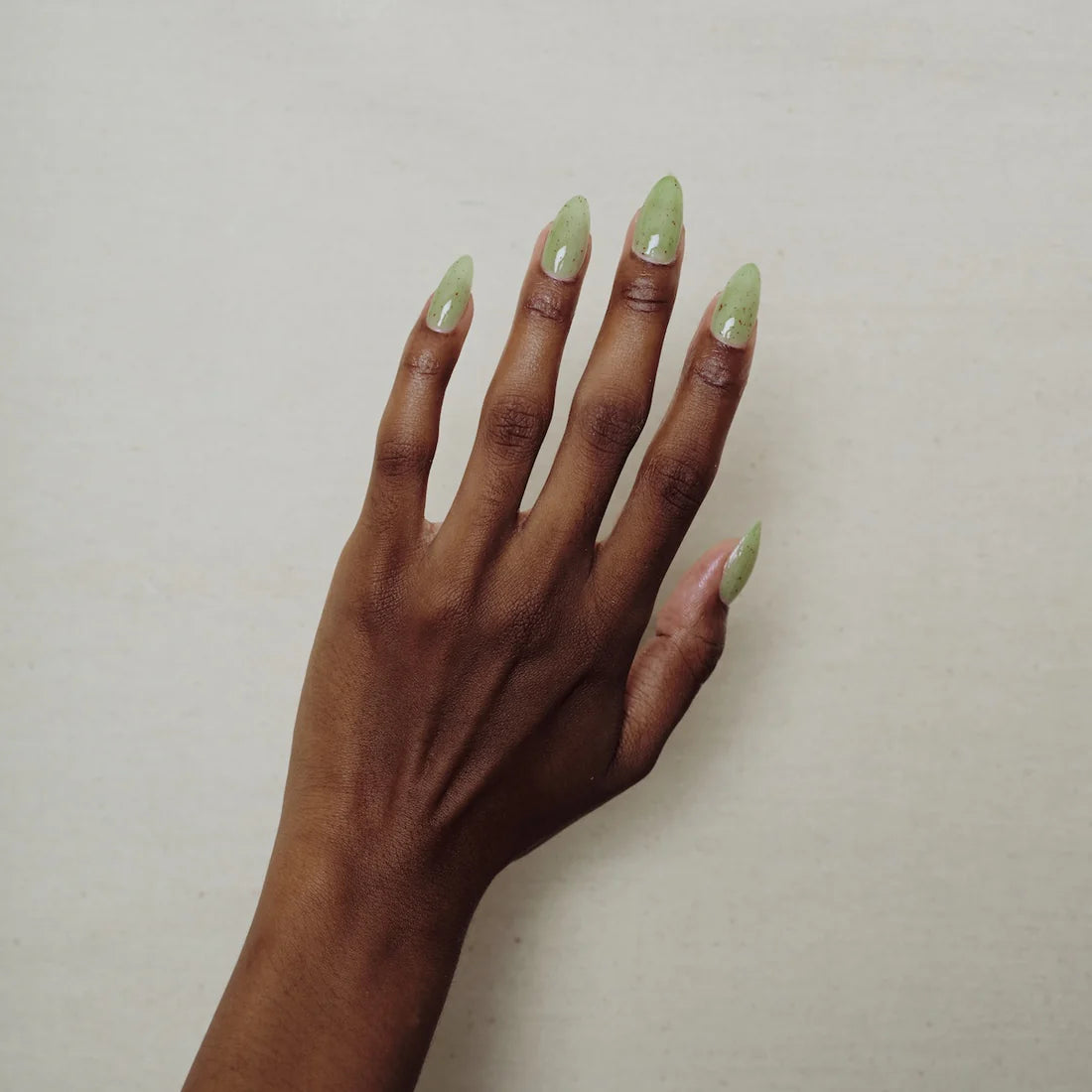 Hand with green nail polish on a plain background