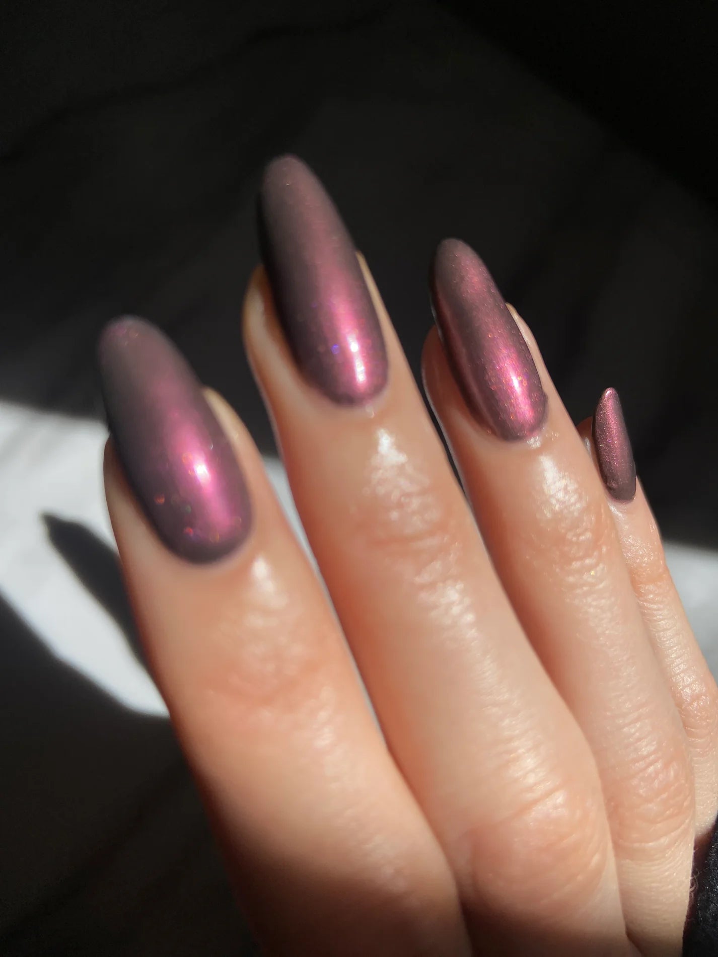 Close up of hand with pink metallic polish on dark background
