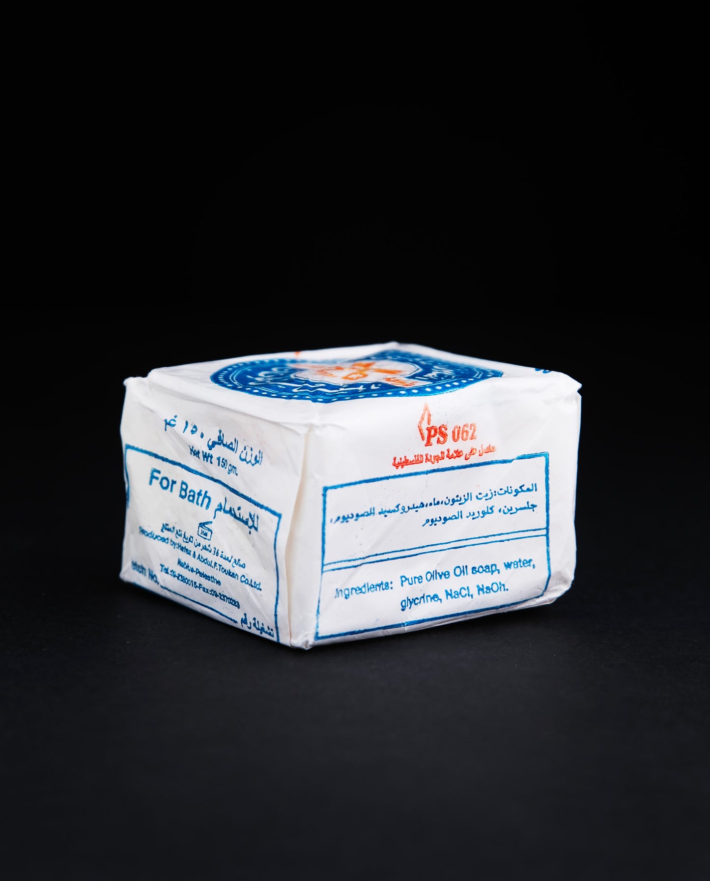 Side view of a bar of Palestinian olive oil soap, wrapped in white wax paper stamped with blue and red
