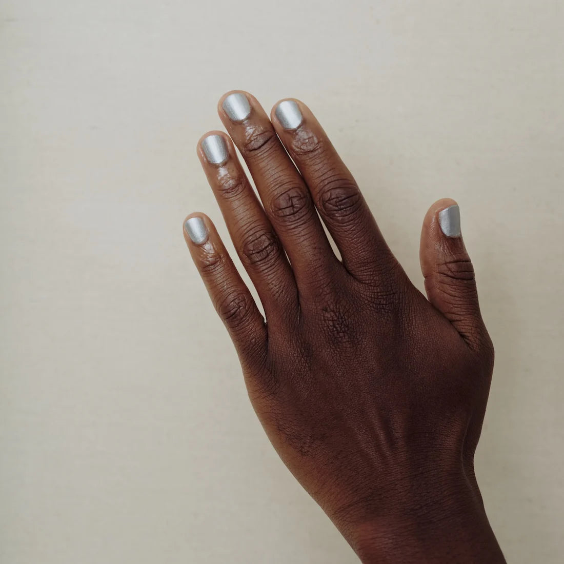 Hand with silver nail polish on a plain background