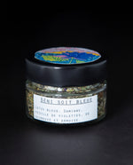 Clear glass jar with black lid containing a blue lotus herbal rolling blend. The white label reads "Béni Soit Bleue"
