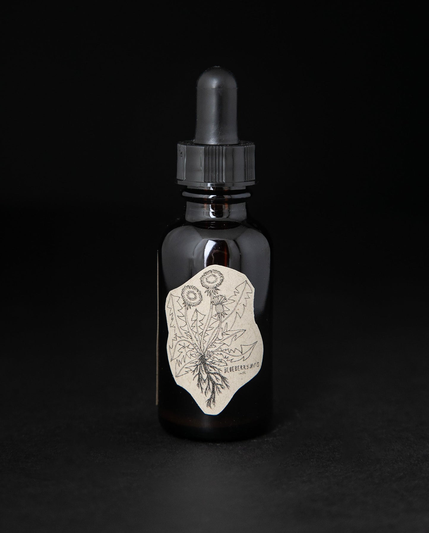 Black glass bottle with dropper top and label featuring a simple line drawing of a dandylion. The bottle contains a herbal tincture by blueberry jams.