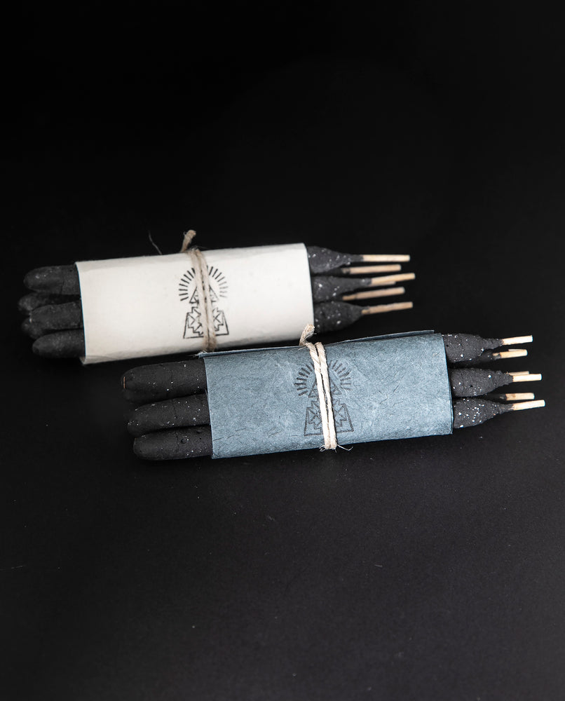 two bundles of Incausa's hand-rolled breu incense sticks wrapped in natural paper and twine, on a black background