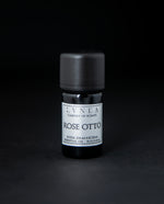5ml black glass bottle of LVNEA's rose otto essential oil on black background