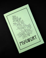 Herbal Revolution's zine about mugwort on black background. The cover is light green, reads "Mugwort" in bold lettering, and features a simple illustration of a mugwort plant.