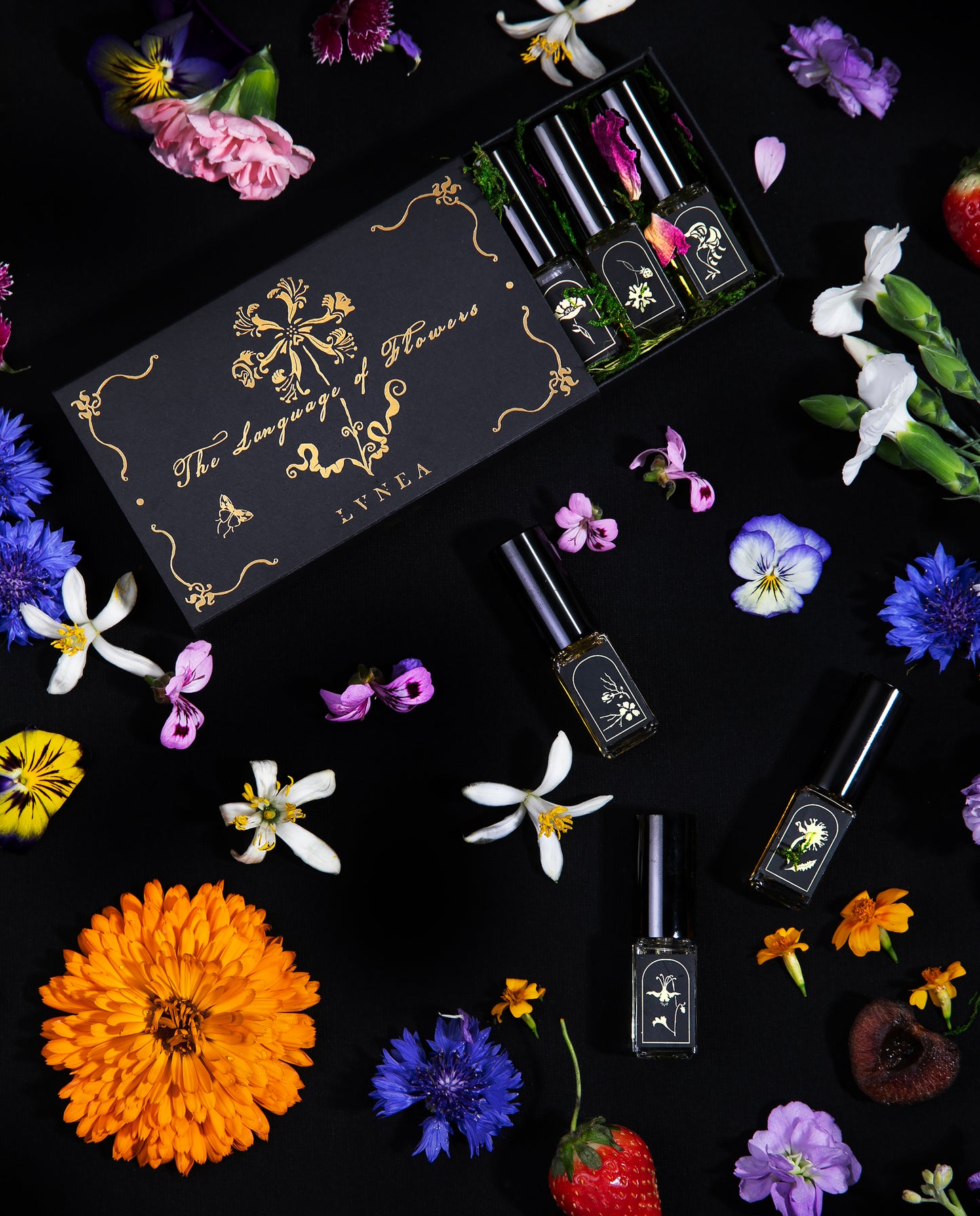 Overhead shot of LVNEA's limited edition "Language of Flowers" eau de parfum box set on a black background surrounded by fresh flowers. 