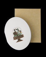 white oval-shaped greeting card sitting atop a hay-coloured enveloppe