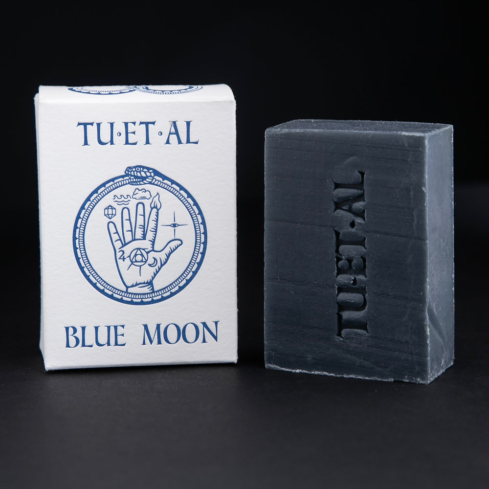 TU-ET-AL's Blue Moon soap next to its white cardboard box against a black background.