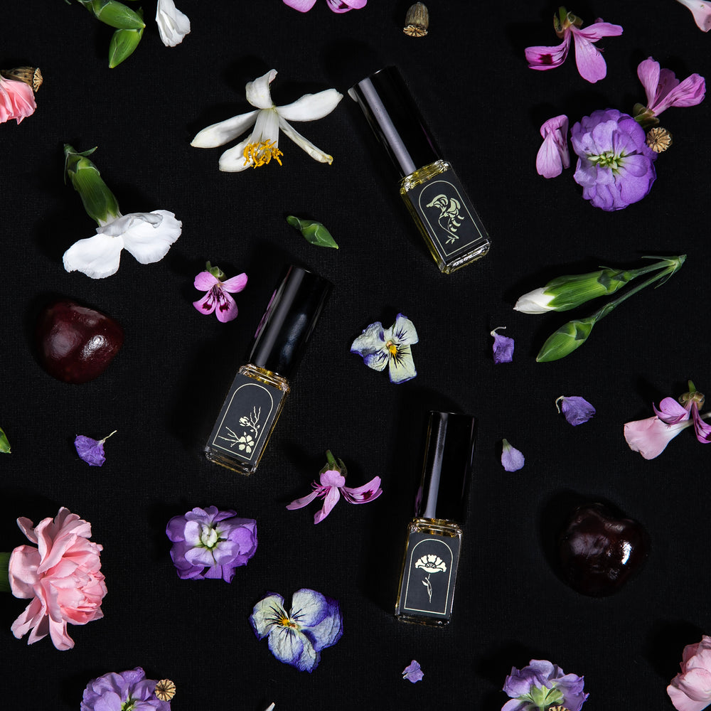 
                      
                        3 mini eau de parfum vials, each labeled with a black and gold foil botanical symbol, surrounded by purple, pink, and white botanicals
                      
                    
