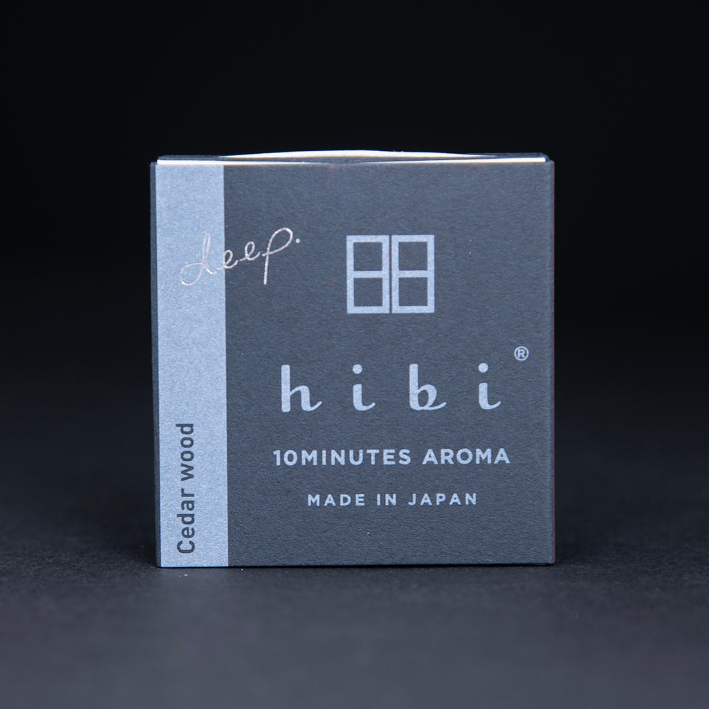 Dark slate grey paper box containing HIBI "cedarwood" incense matches, sitting on black background
