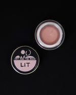 Glass jar of Fat and the Moon's "Lit" highlighter, open to reveal a shimmering dusty rose.