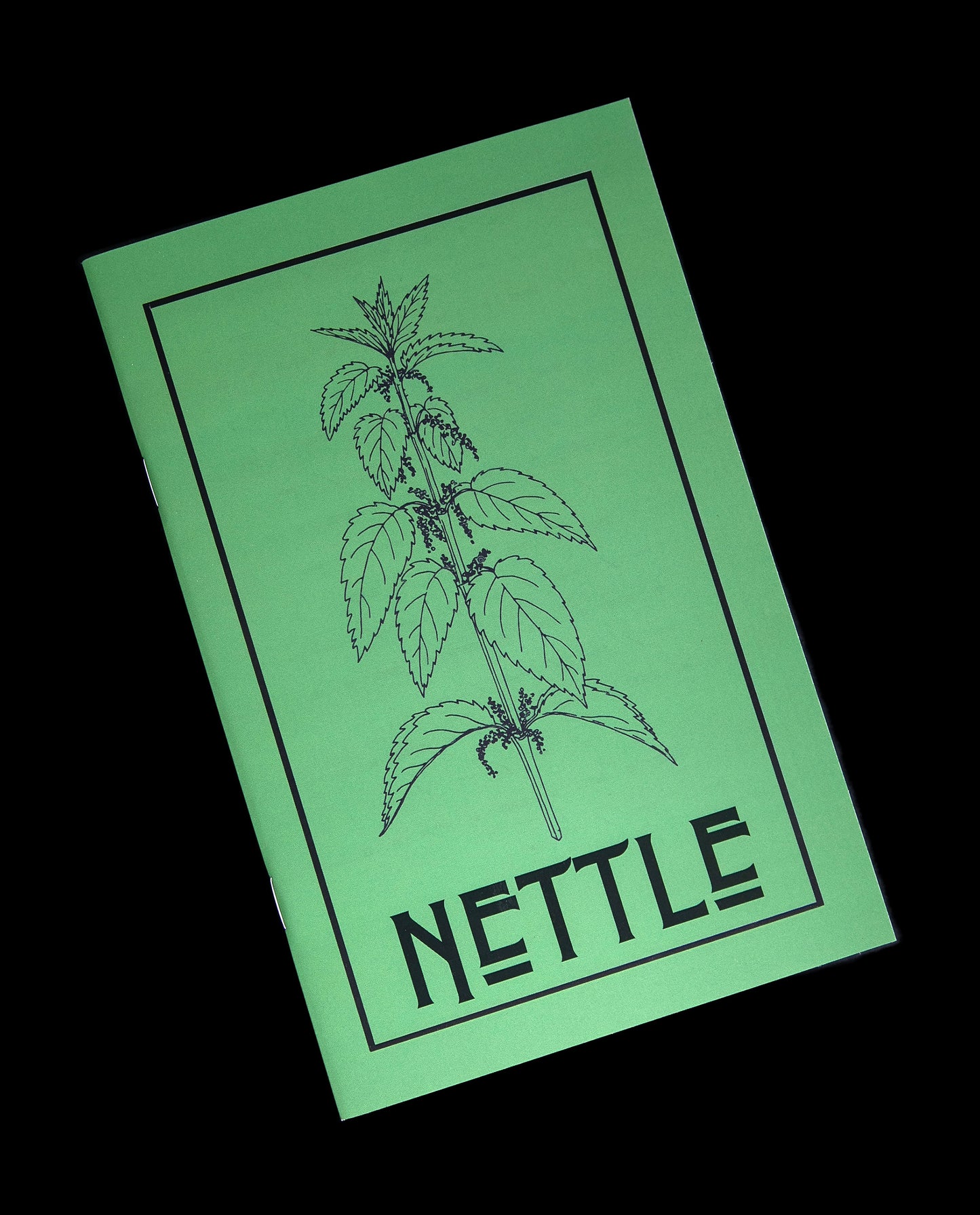 Front view of Herbal Revolution's "Nettle" zine on black background. The cover is green with a botanical illustration of nettle, and the word "NETTLE" written in large black letters on the front.