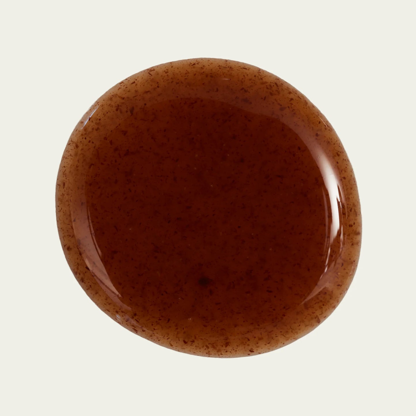 Swatch of "reishi" nail polish against cream background. The polish is a warm transparent brown with visible flecks of real reishi mushroom mixed throughout.