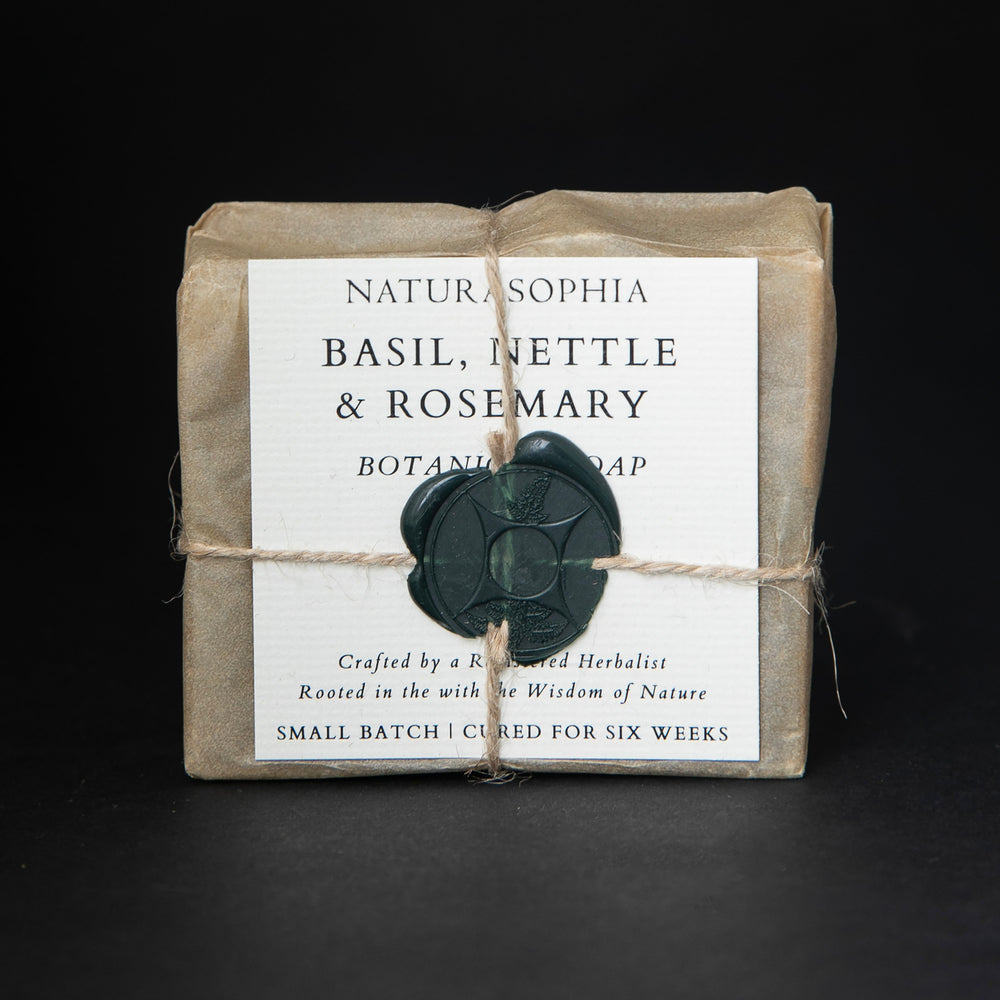 Bar of Naturasophia soap wrapped in brown paper and twine, with a label that reads "Basil, Nettle & Rosemary". There is a deep green wax stamp holding the label in place.