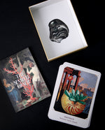 Overhead shot of The Seashell Oracle Deck booklet a stack of cards, and the inner box, each featuring collages of vintage illustrations, scattered on a black surface.