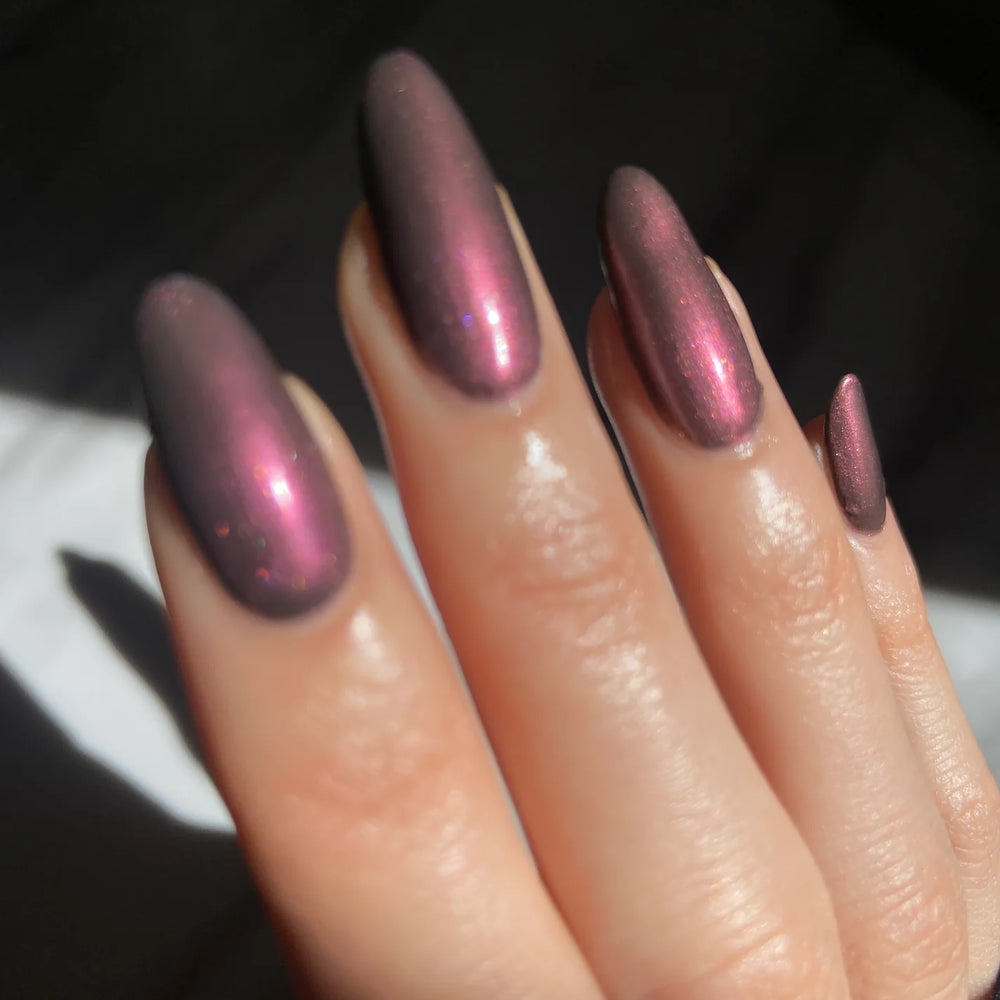 
                      
                        Close up of hand with pink metallic polish on dark background
                      
                    