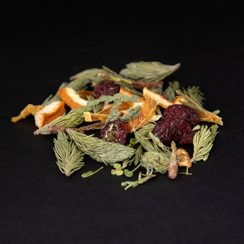 a handful of loose lead "Solstice" herbal tea against a black background. This colourful blend features dried cranberries, spruce tips, and dried orange slices.