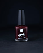 "Swamp Sparrow" nail polish by Death Valley Nails on black background. The polish is a deep cherry red colour with a jelly finish.
