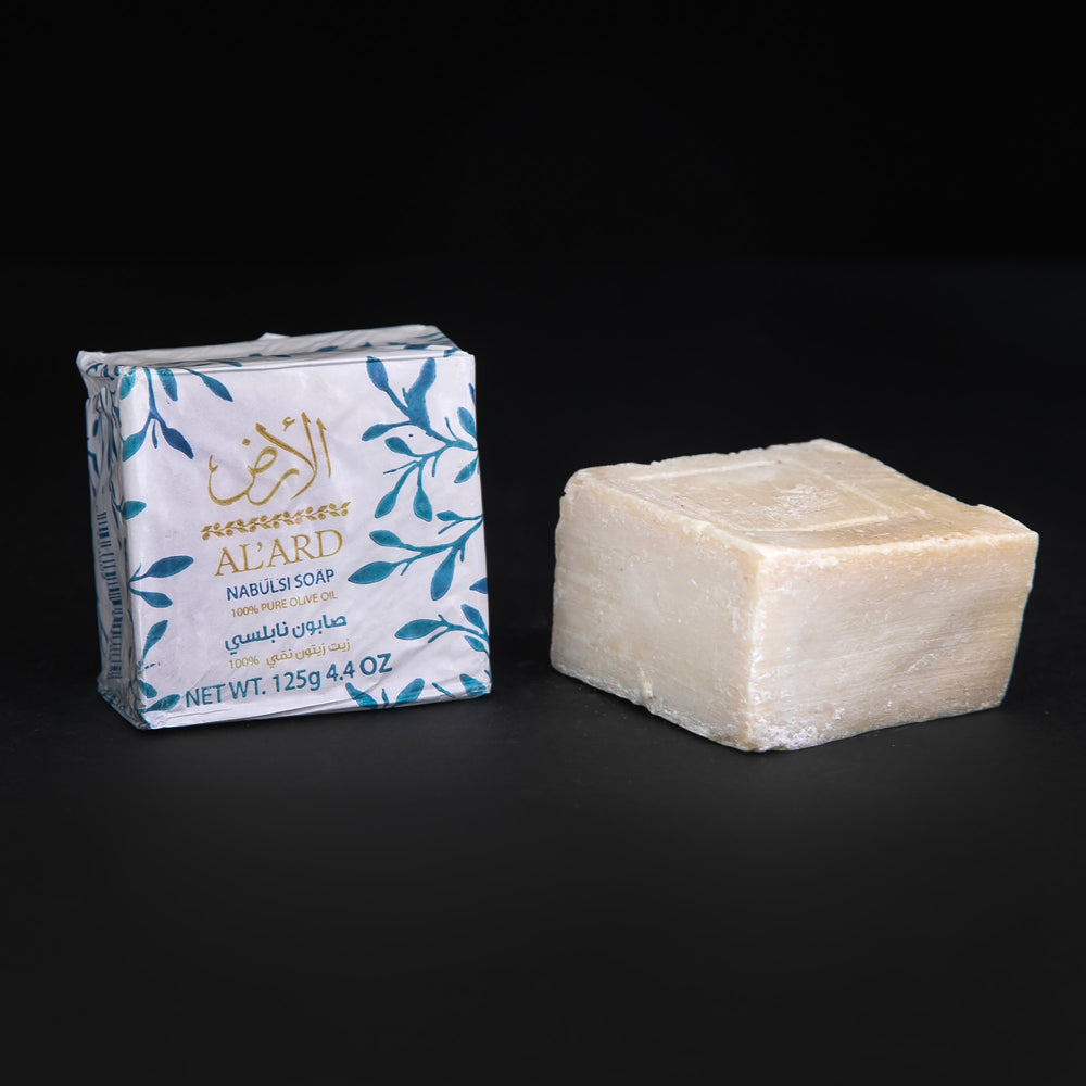 Wax paper-wrapped bar of olive oil soap next to unwrapped bar of soap. sitting on black background
