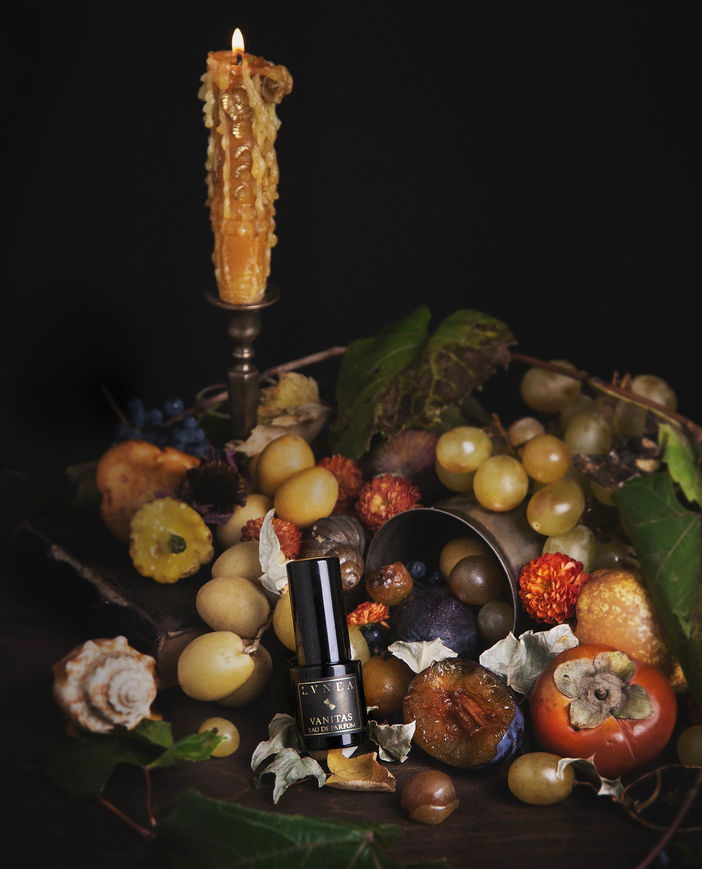 Fruit bowl with a candle and a bottle of perfume on a dark background