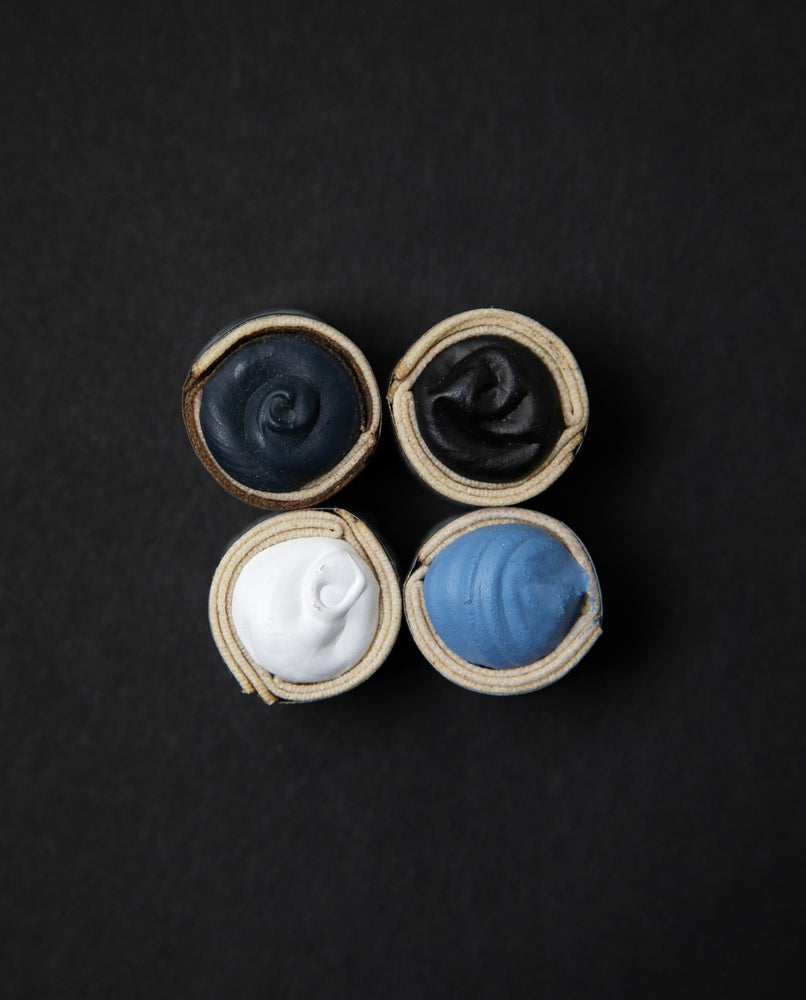 Four Beam Paints watercolour paintstones in slate grey, black, white, and blue presented on a black background.