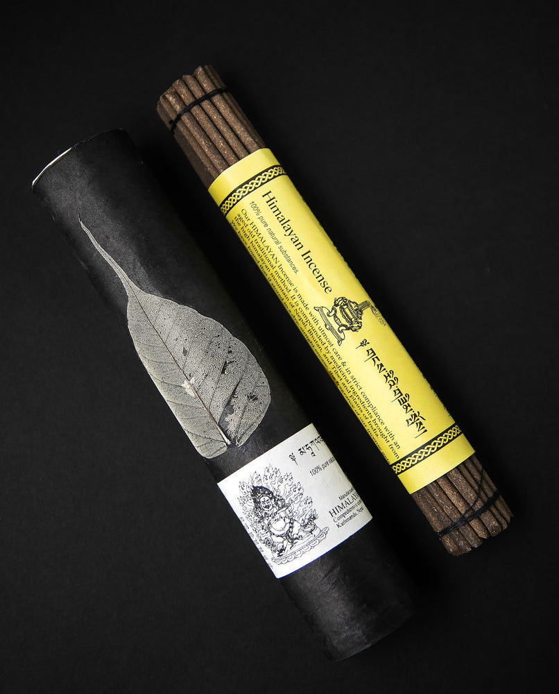 A bundle of incense sticks bound in yellow paper, sitting next to a black paper tube with a bodhi leaf pressed onto it.