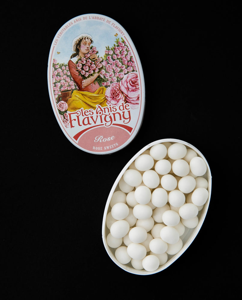 Open tin of rose flavoured bonbons. There is an illustration of a woman in a field of roses on the top of the tin.