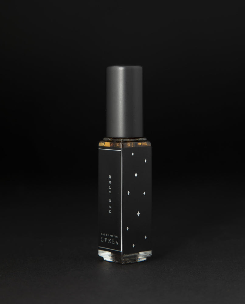 8ml clear glass bottle of LVNEA’s Holy Oak natural perfume on black background, bottle is rotated at a 3/4 angle exposing a star pattern on the label.