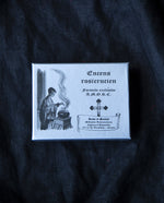 Silver box of Rose & Sandalwood Rosicrucian incense on black fabric background.