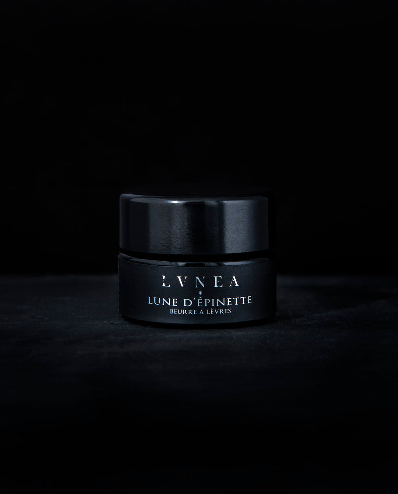 A rich, botanical lip butter made by LVNEA and housed in a black 5g glass pot. The label reads "LUNE D'ÉPINETTE" on it in silver. The product is natural smells lightly of cardamom, spruce, and vanilla.