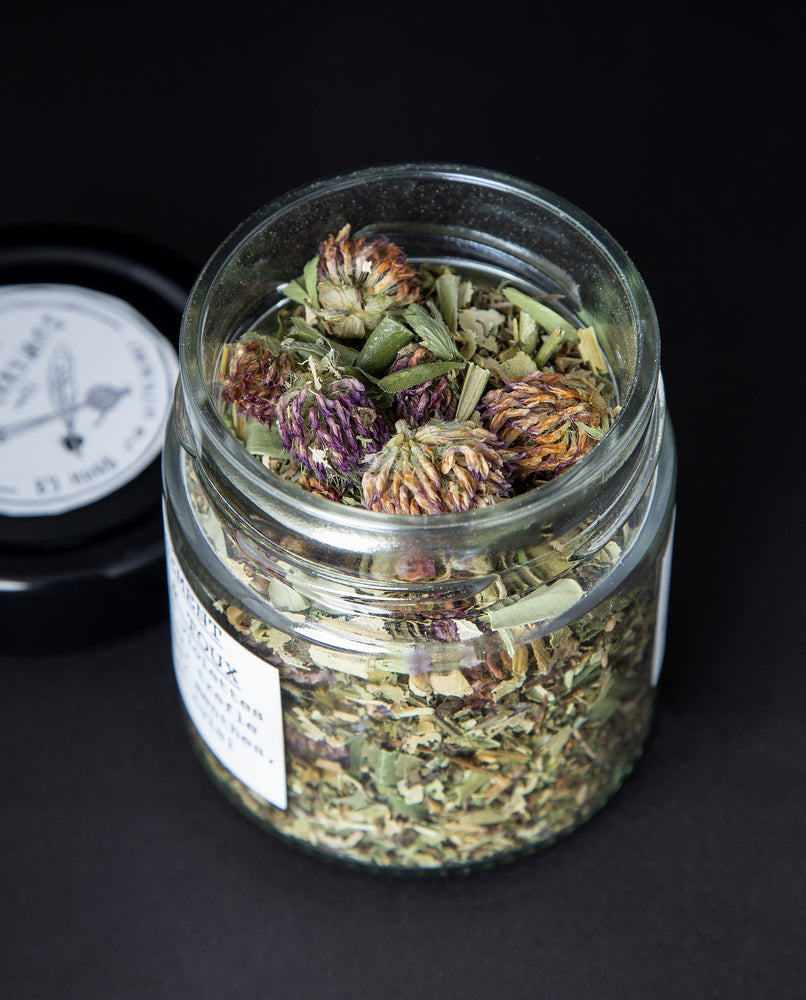 Clear glass jar with lid removed, revealing a herbal tea blend where red clover buds feature prominently.
