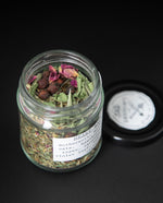 clear glass jar with black lid containing "heart balm" herbal tea blend by blueberryjams. The jar is turned to show the french label which reads "Baume Pour Le Coeur"