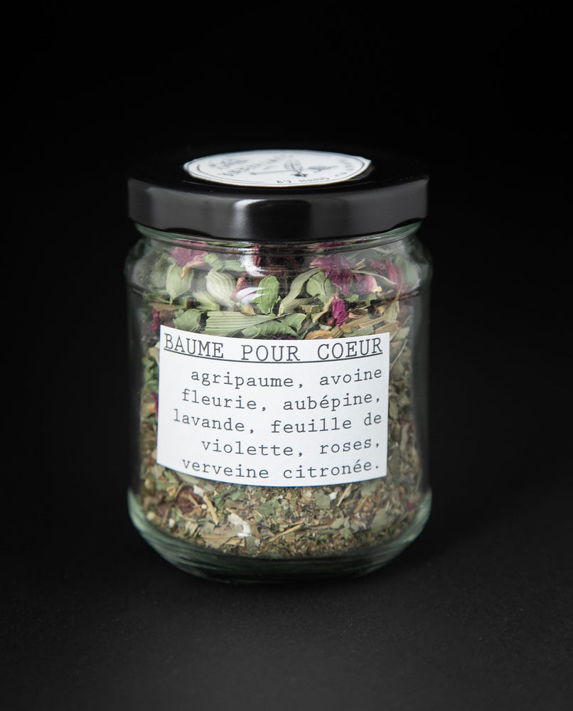 clear glass jar with black lid containing "heart balm" herbal tea blend by blueberryjams. The jar is turned to show the french label which reads "Baume Pour Le Coeur"