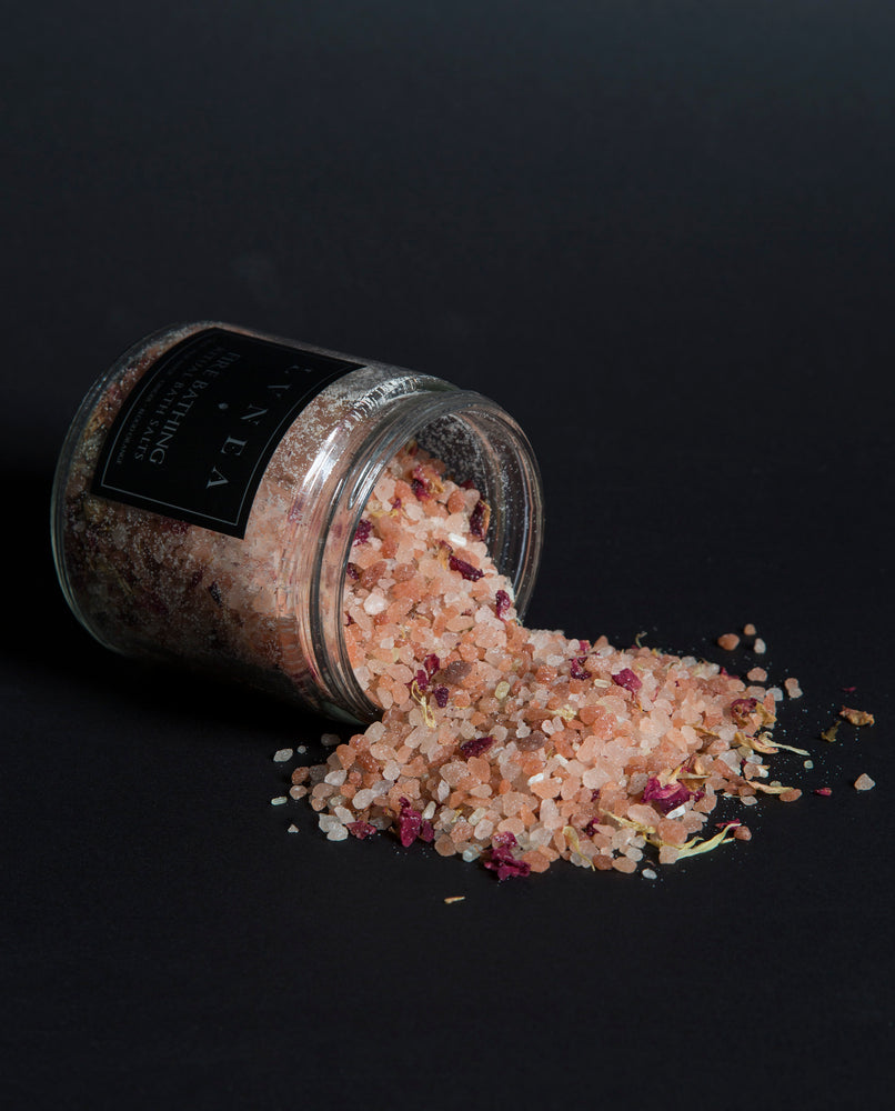 LVNEA'S rose-hued Fire Bathing bath salts spilling out of a tipped over 16 ounce clear glass jar
