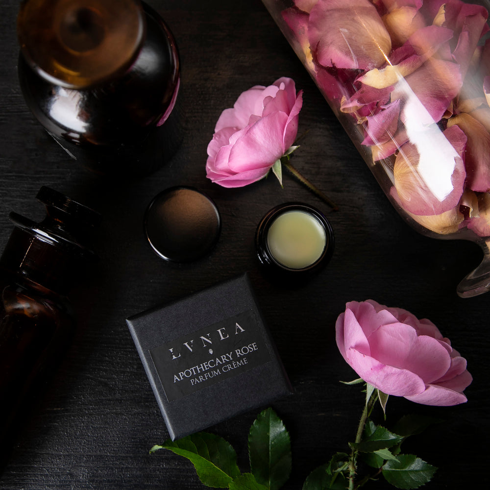 
                      
                        overhead view of opened jar of solid perfume next to fresh roses and apothecary jars
                      
                    
