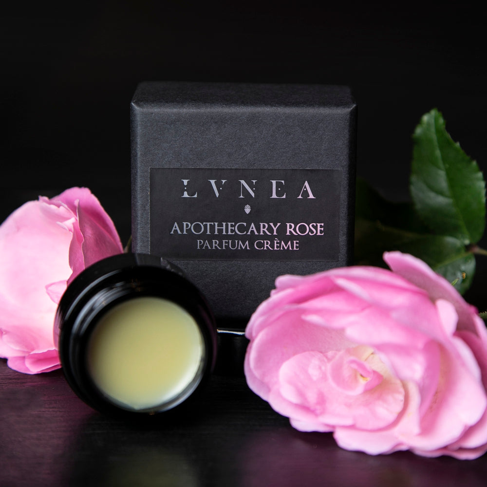 
                      
                        Opened black glass jar of Apothecary Rose solid perfume and black box next to roses on a black wood surface
                      
                    