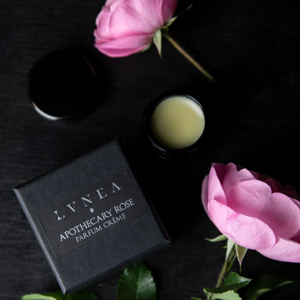 
                      
                        Opened black glass jar of LVNEA'S Apothecary Rose solid perfume and black box next to roses on a black wood surface
                      
                    