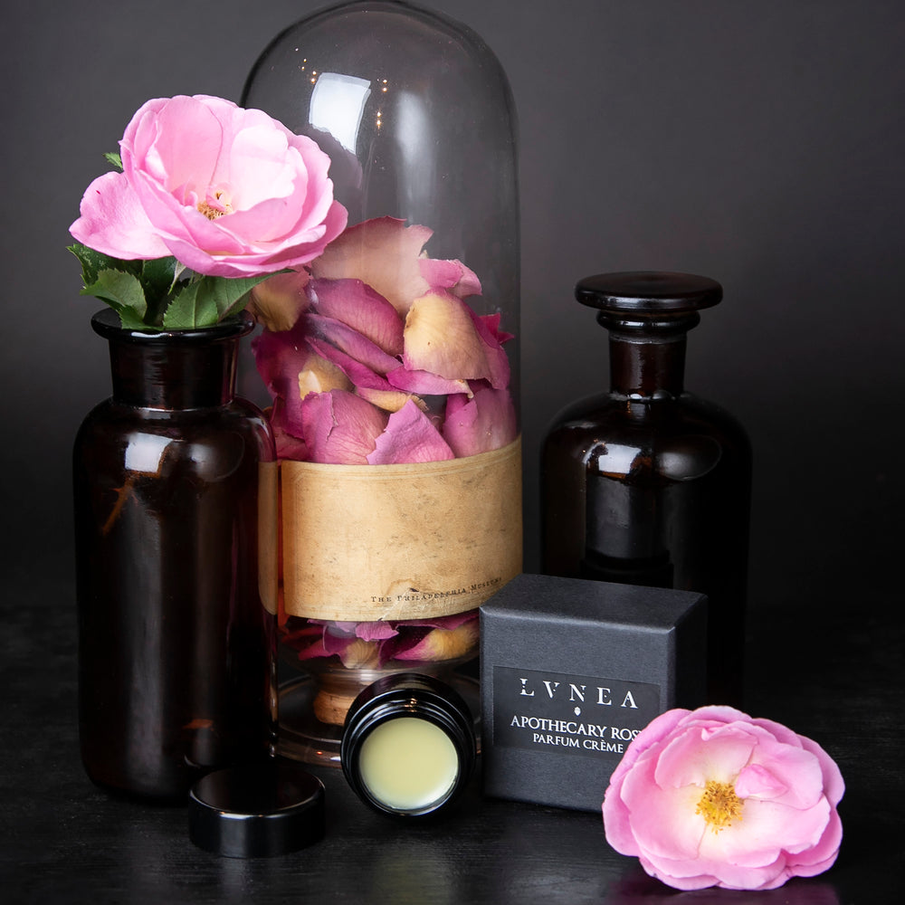 
                      
                        10g jar of solid perfume next to fresh roses and apothecary jars on black surface
                      
                    