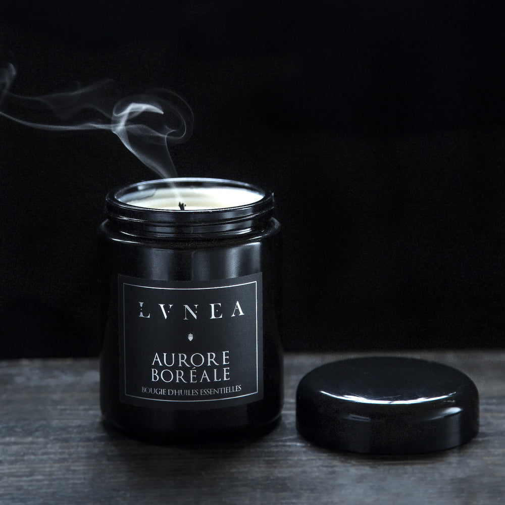 Aurore Boréale candle housed in a resealable 8 ounce black glass jar. The lid is open revealing a wisp of smoke emerging from the just-extinguished cotton wick.