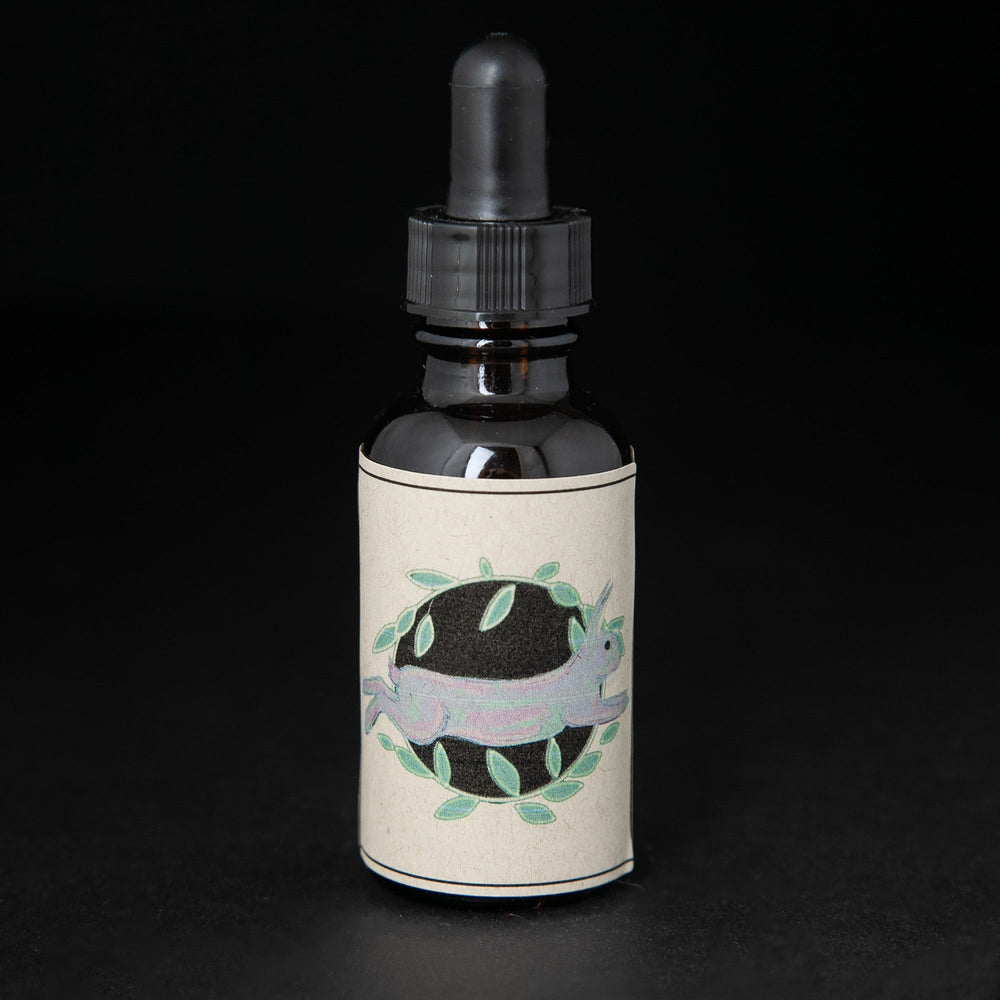 Black glass bottle with dropper top of blueberryjams' "Secret Garden" herbal tincture. The label on the bottle has an illustration of a rabbit surrounded by leaves. 