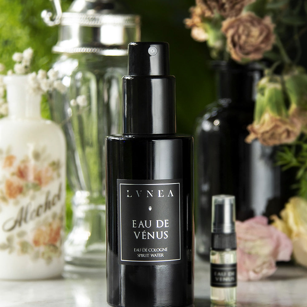 100ml black bottle and sample vial of LVNEA'S Eau de Venus fragrance sitting on white marble surrounded by pink florals