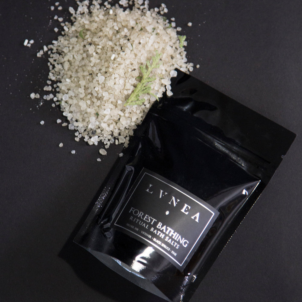 4oz black resealable pouch of LVNEA's Forest Bathing bath salts with a mound of green-hued salt next to it