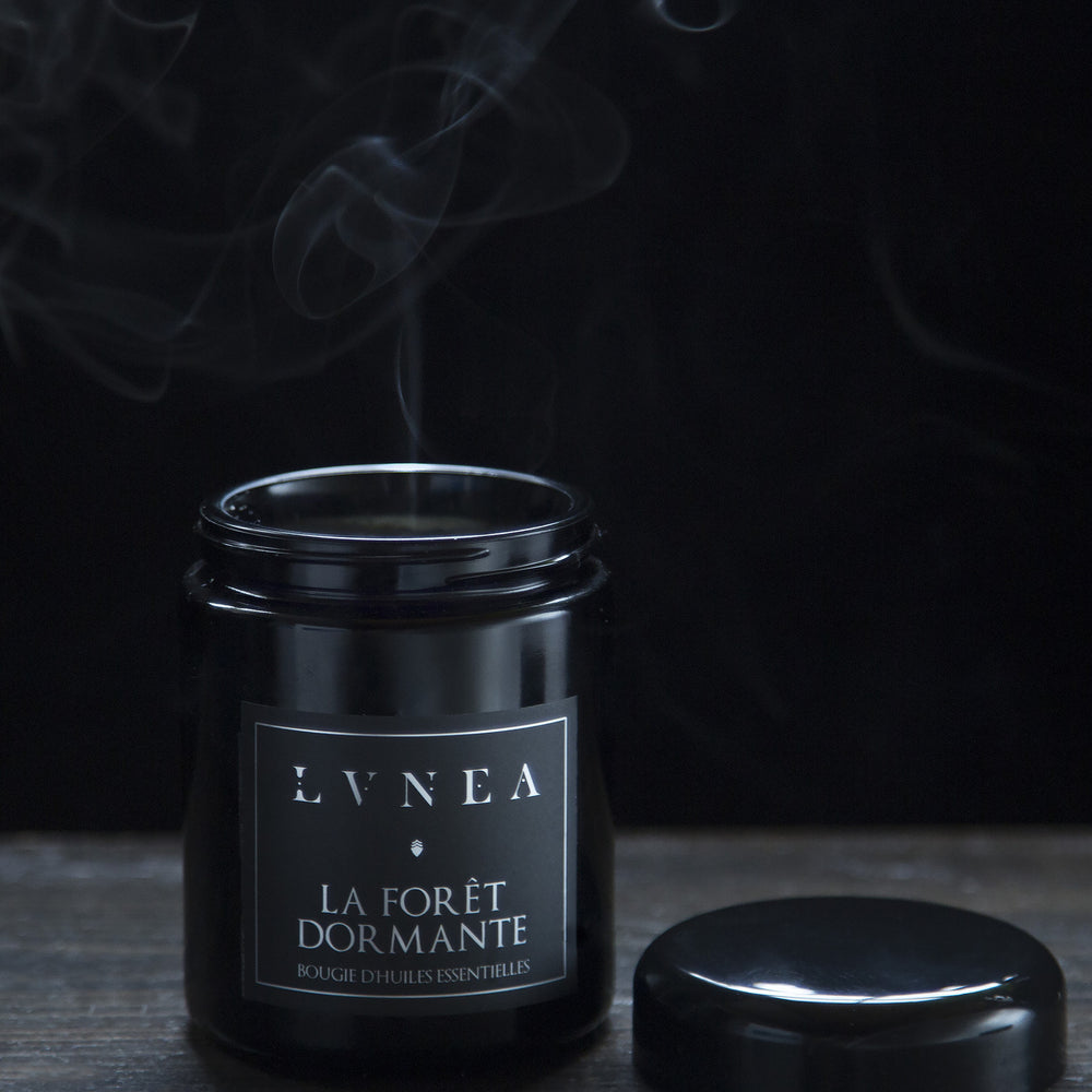 La Foret Dormante candle in an 8oz black jar with lid removed. A plume of smoke is coming out from the top of the candle.