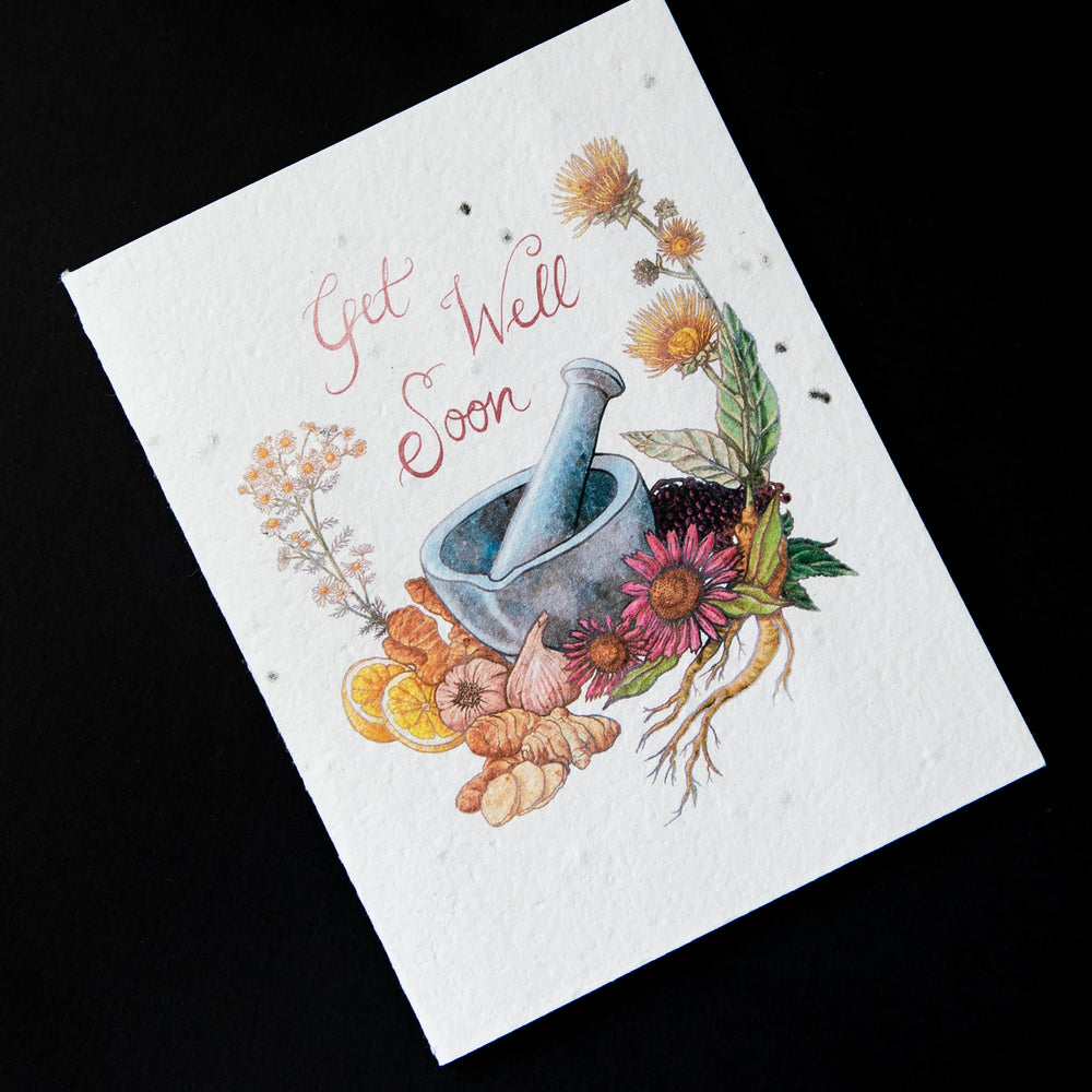 Cream coloured greeting card with illustration of a mortar and pestle surrounded by botanicals. The card reads "get well soon". The cardstock is textured and studded with seeds.