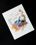 Cream coloured greeting card with illustration of a mortar and pestle surrounded by botanicals. The card reads "get well soon". The cardstock is textured and studded with seeds. 