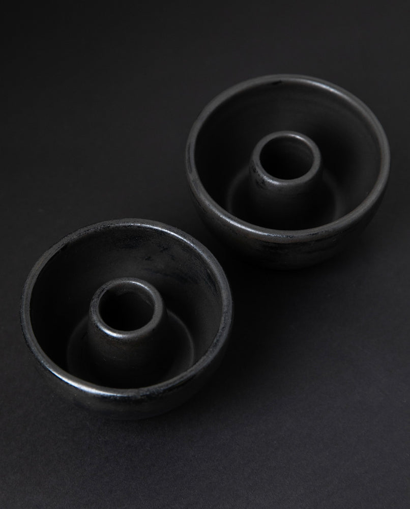 two matte charcoal-coloured stoneware candle holders on black background from 3/4 angle