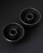 two matte charcoal-coloured stoneware candle holders on black background from 3/4 angle
