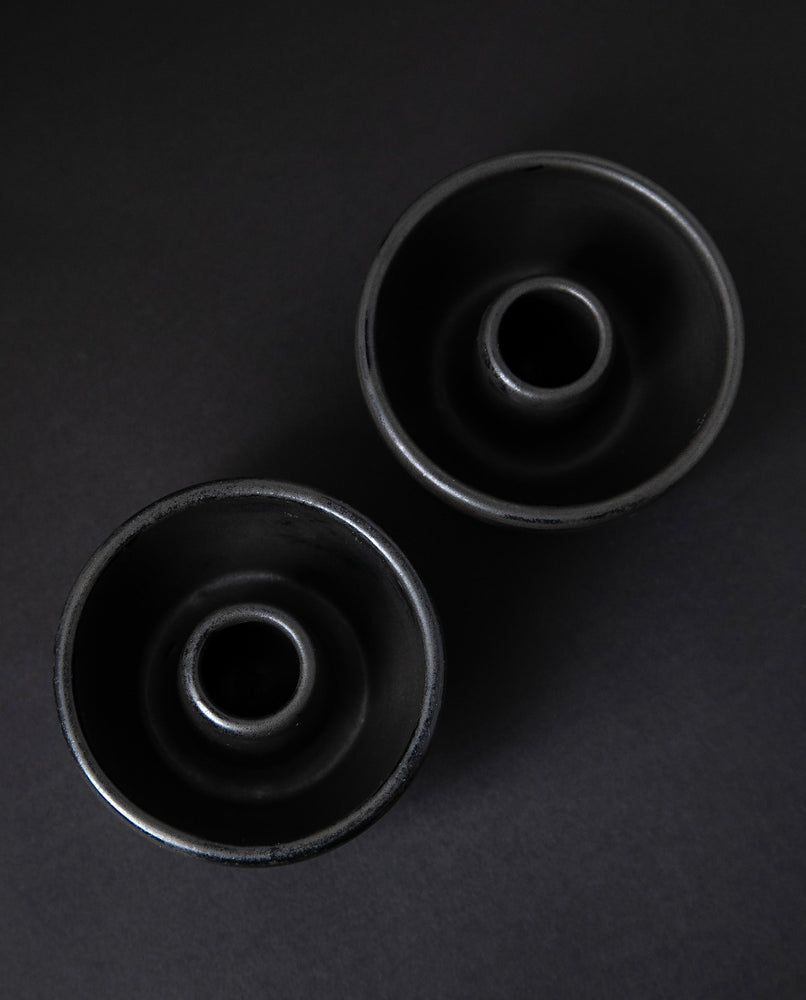 two matte charcoal-coloured stoneware candle holders on black background from top down angle