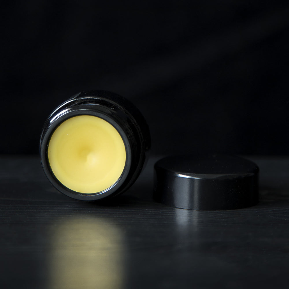 LVNEA's Midnight Tuberose solid perfume on black background. The 10g black glass pot is open and reveals a golden cream perfume.